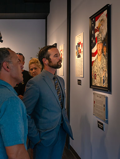 Visitors reading a fallen hero's portrait plaque inside the Portrait of a Warrior Gallery